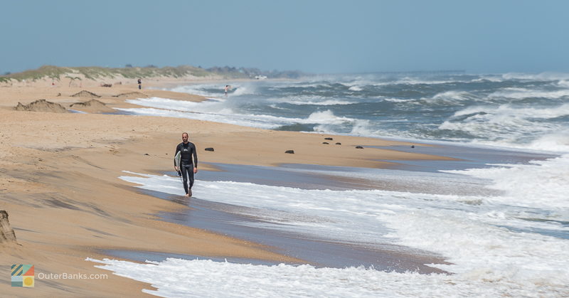 A surfer strolls along the beach in Buxton NC