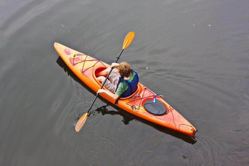 A boy kayaking with a fishing pole