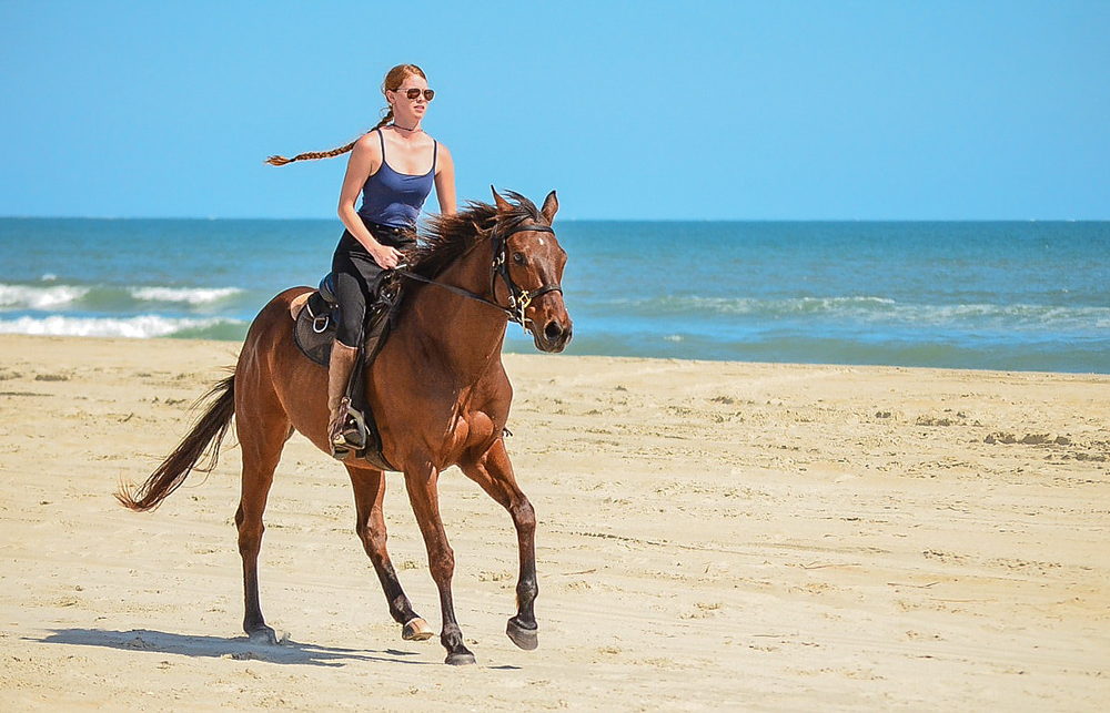 A woman riding along the beach  with Equine Adventures