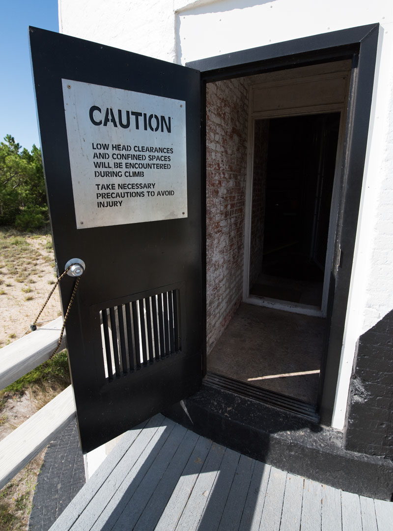 Door with caution sign as visitors enter to climb the Cape Lookout Lighthouse.