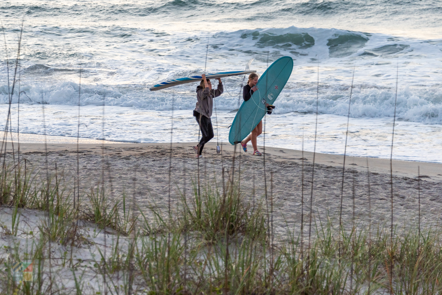 Surfers walk to the water at sunrise
